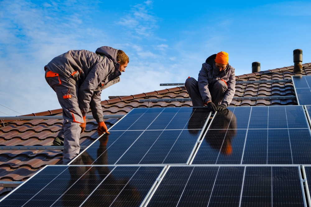 Two workers installing solar panels on a residential rooftop on a sunny day.